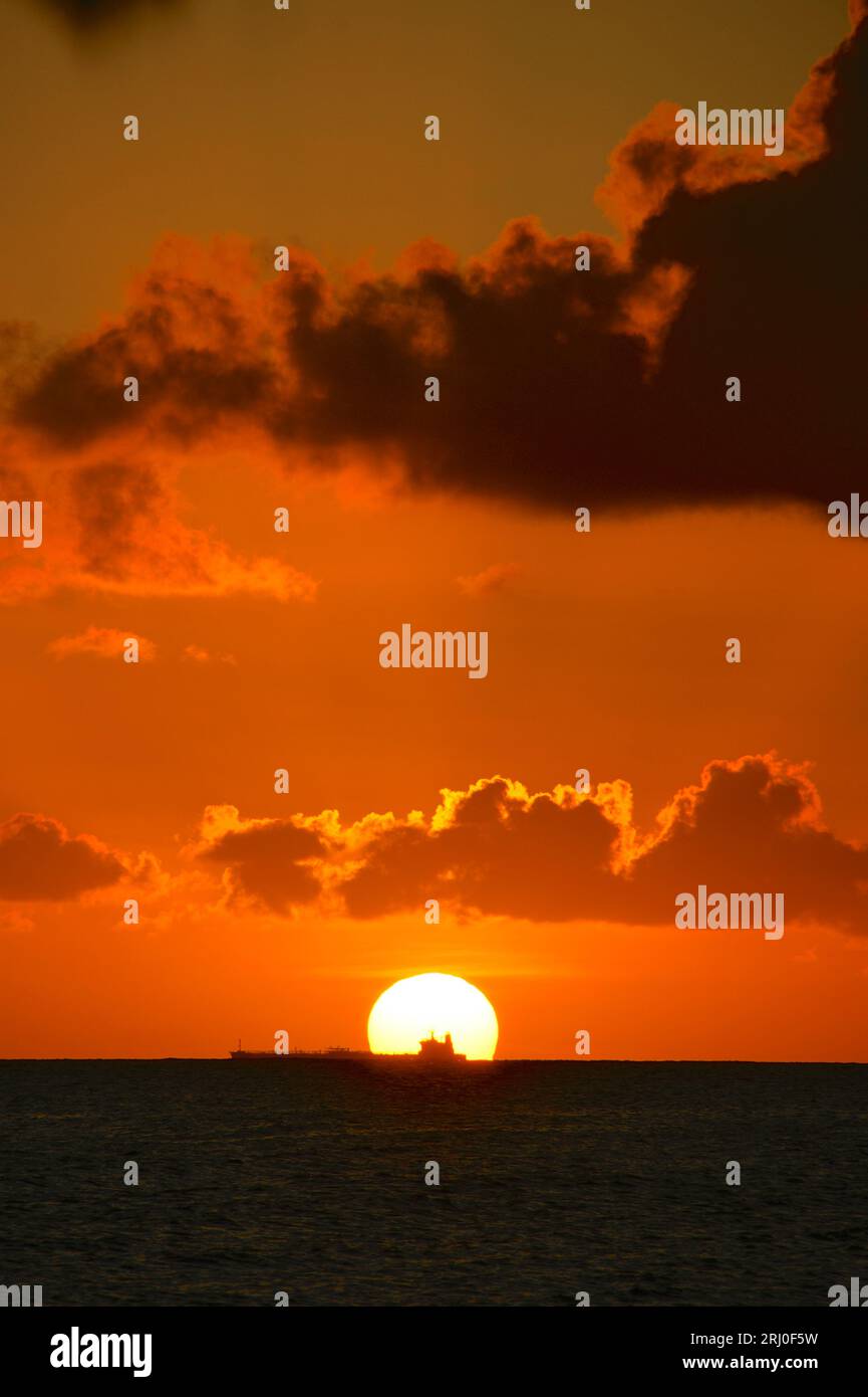 Das Seeschiff passiert den Sonnenuntergang zwischen Curacao und Venezuela; schwarzes Meer und orangefarbener Himmel mit einigen Wolken Stockfoto