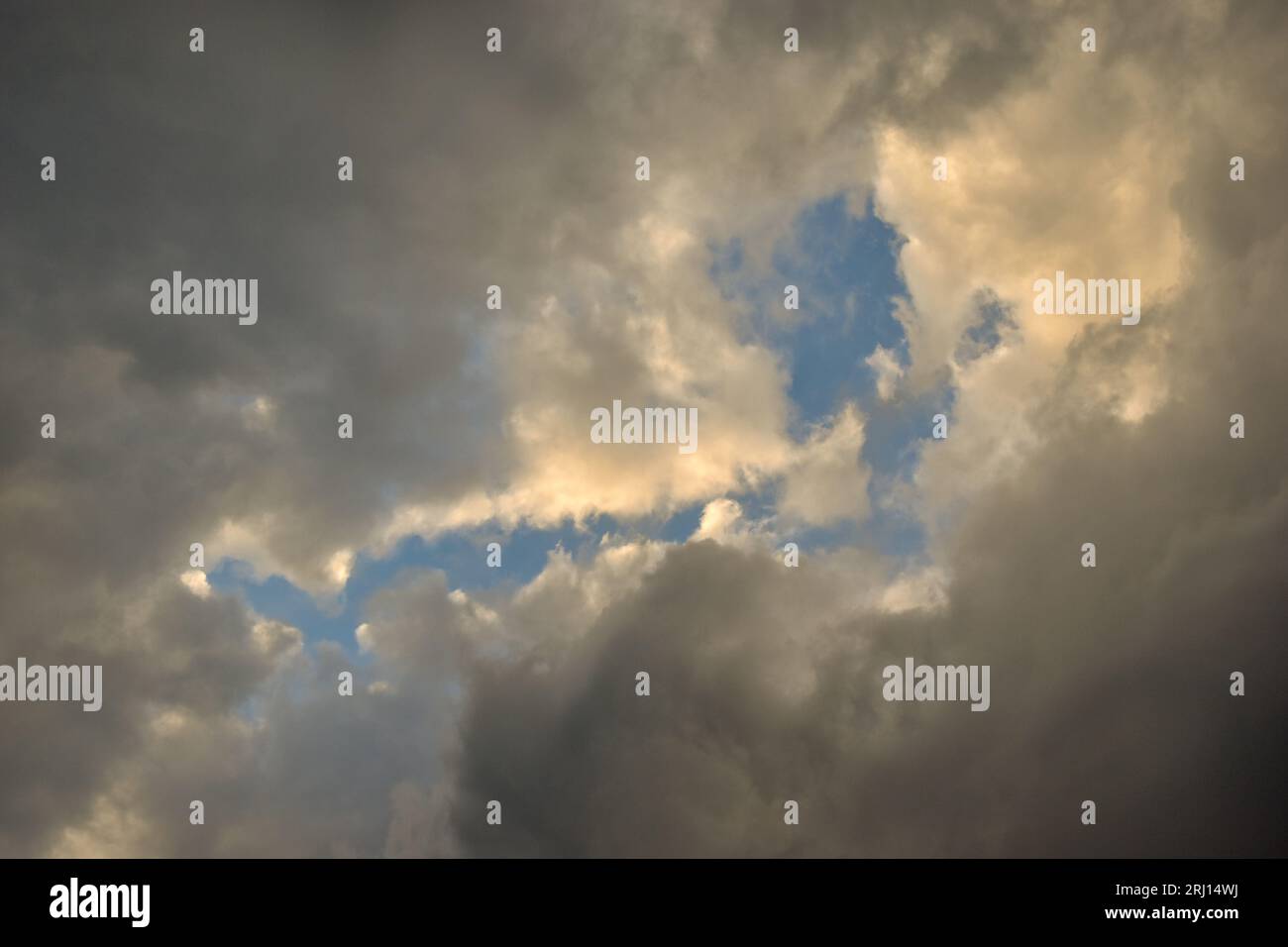 Blauer Himmel, der durch eine Lücke in einigen dunklen Wolken schaut. Stockfoto