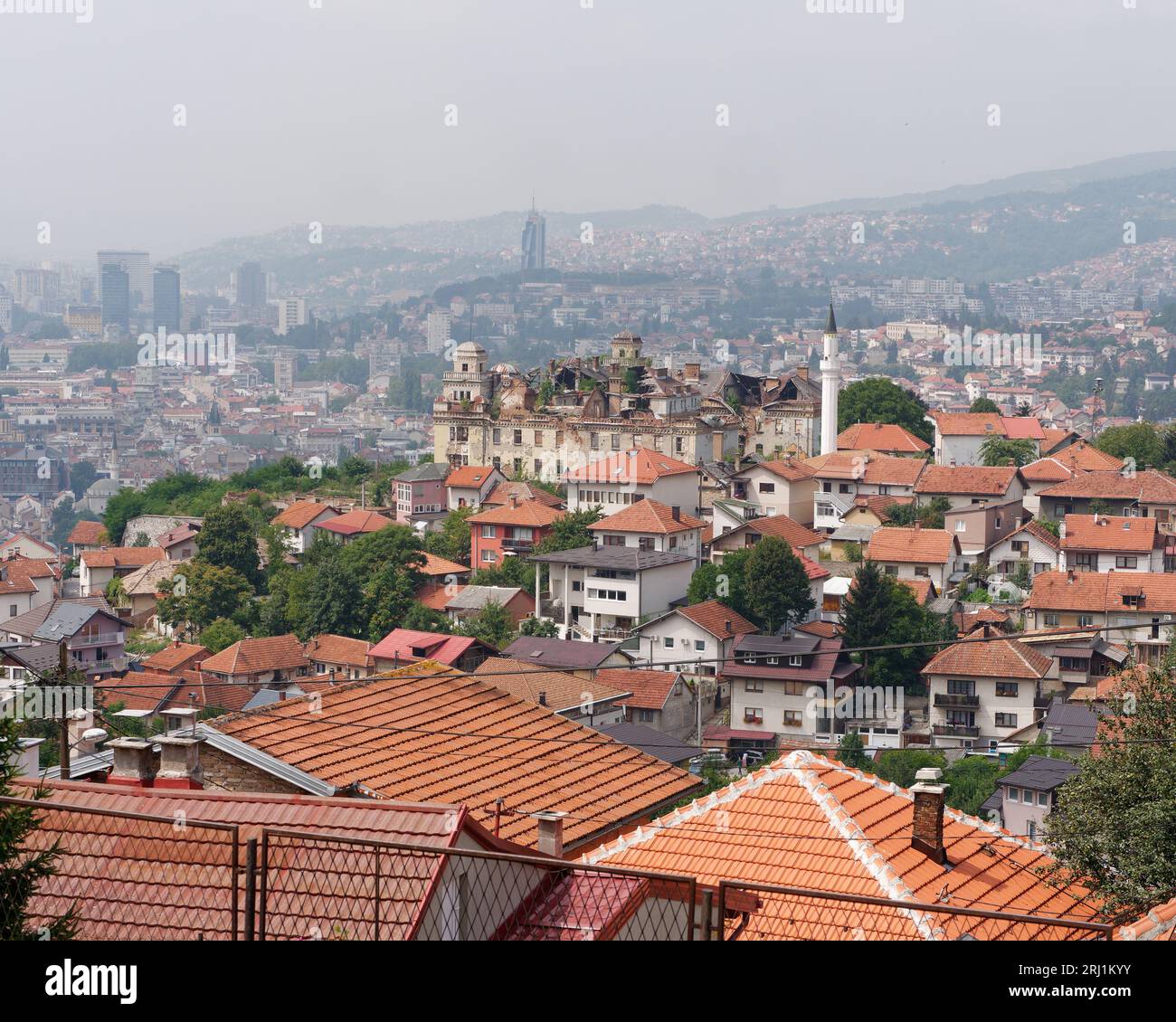 Erhöhter Blick über die Dächer in Sarajevo, Bosnien und Herzegowina, 19. August 2023. Großes Herrenhaus mit beschädigtem Dach auf dem Hügel. Stockfoto