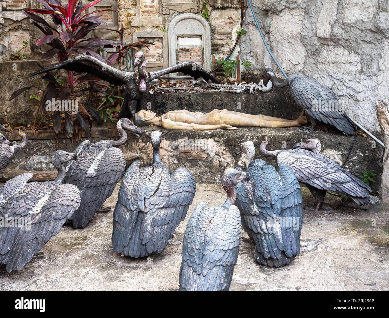 Ein unheimliches Tableau entfaltet sich im Wat Saket, dem Goldenen Berg Bangkoks, während Geierstatuen den Blick in eine leblose Form lenken und eine makabre Szene fesseln. Stockfoto
