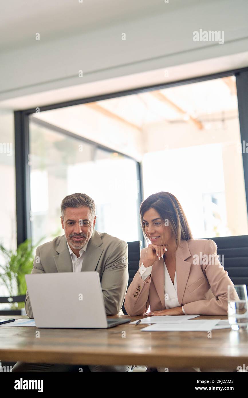 Zwei glückliche Geschäftsleute, die im Büro arbeiten und sich ein Notebook ansehen. Stockfoto