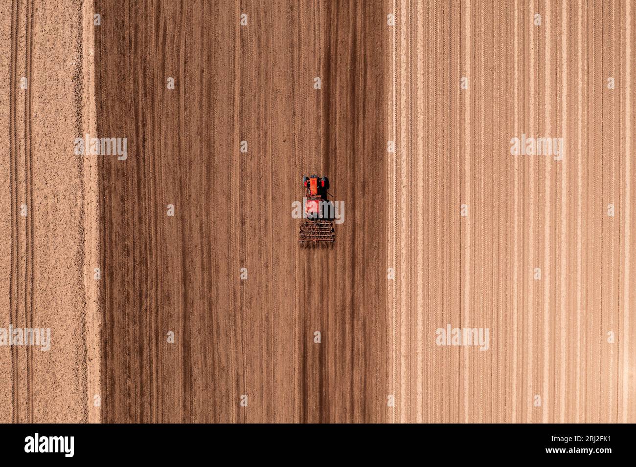 Roter landwirtschaftlicher Traktor mit angebauter Deichsel, der vor der Aussaat die Bodenbearbeitung durchführt, Luftaufnahme vom Drohnen-pov von oben nach unten Stockfoto