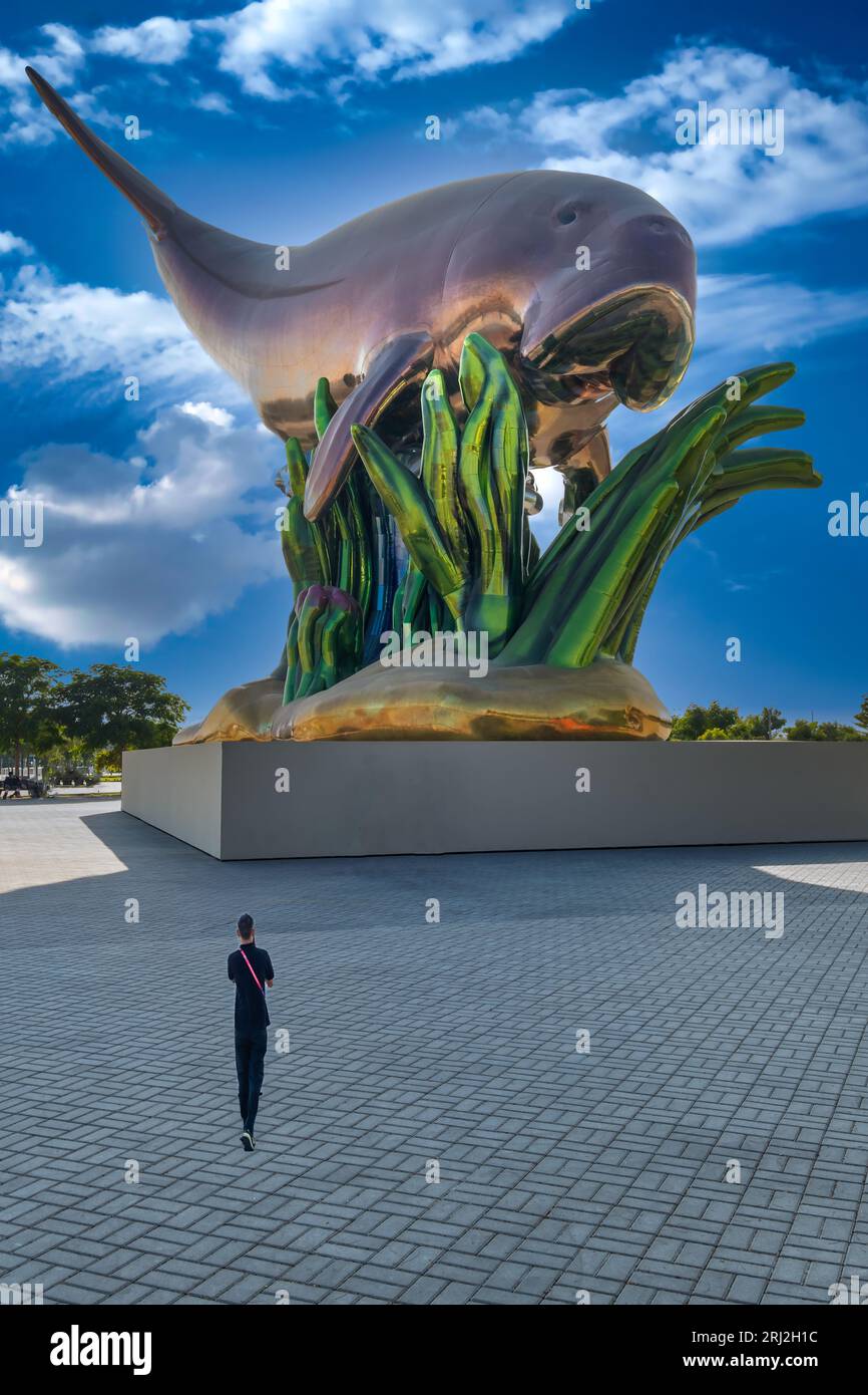 Der FIFA WC-Anhänger von Katar posiert in der Nähe einer riesigen Walstatue, die von den bezaubernden Wolken und dem warmen Licht des Sonnenuntergangs eingerahmt wird. Stockfoto