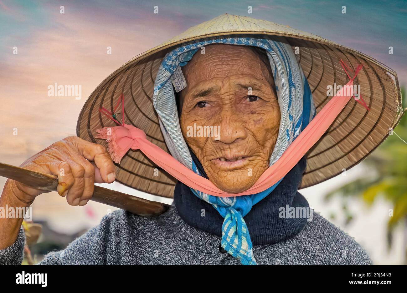 Hoi-An, Vietnam - 9. Dezember. 2014: Porträt einer alten, Reifen, armen vietnamesischen Bäuerin, sonnengebräuntes, faltiges Gesicht, traditioneller Kegelhut mit Heav Stockfoto