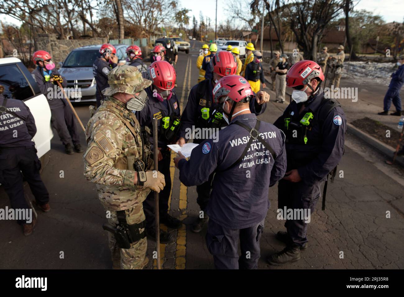 Ein US Border Patrol Agent, links, koordiniert sich mit Mitgliedern des Urban Search and Rescue Teams der Federal Emergency Management Agency, bevor er in Lahaina, Hawaii, am 17. August 2023 durch verbrannte Trümmer kämpft. CBP-Foto von Glenn Fawcett Stockfoto