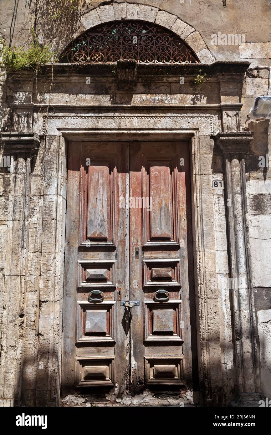 Alte Wetter Holztür mit Steinbogen Sturz in einem verlassenen alten Herrenhaus in der Altstadt von Rethymno, auf der Insel Kreta, Griechenland, Europa. Stockfoto