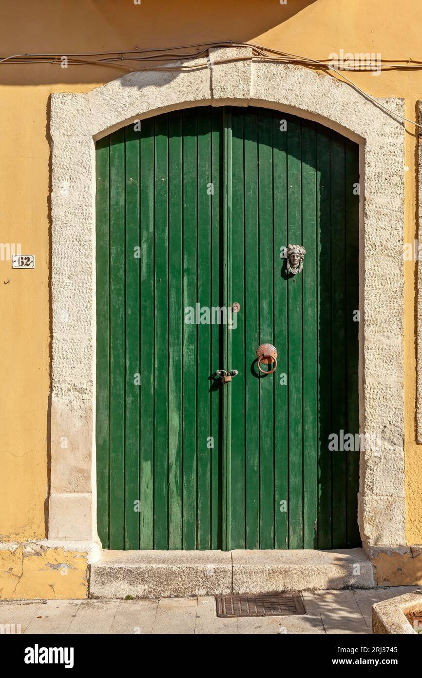 Wunderschöne alte, grüne Holztür im traditionellen Stil, mit Steinrahmen und Türsturz und gelber Wand im warmen Nachmittagslicht, im Dorf Archanes. Stockfoto
