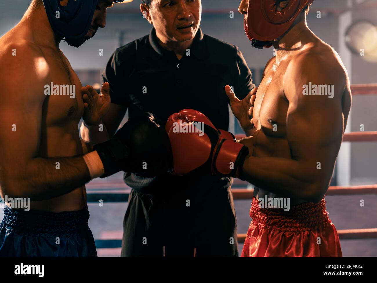 Ein Boxer mit Schutzhelm oder Kopfschutz zeigt sich aneinander, während der Schiedsrichter dem Gegner die Regeln für die Interaktion erklärt, bevor er mit dem Boxkampf beginnt Stockfoto