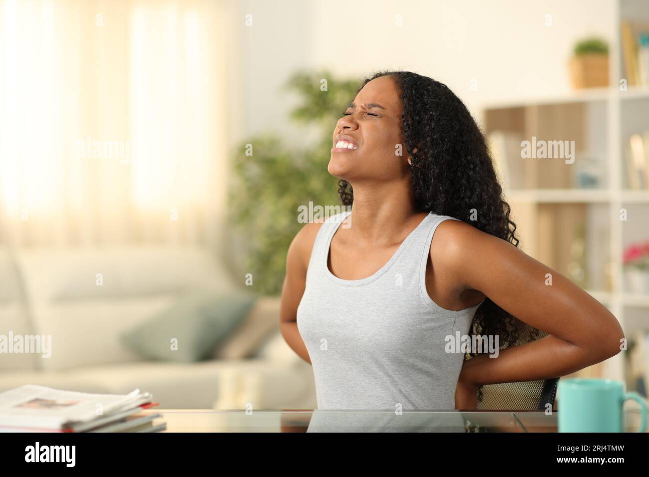 Schwarze Frau, die Rückenschmerzen hat, sitzt zu Hause auf einem unbequemen Stuhl Stockfoto