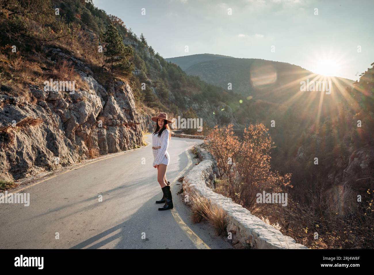 Der Berg der Weiberstraße. Eine Frau in einem weißen Pullover, schwarzen Stiefeln und einem Hut wandert bei Sonnenuntergang auf einem gewundenen Bergweg zwischen den Bergen Stockfoto