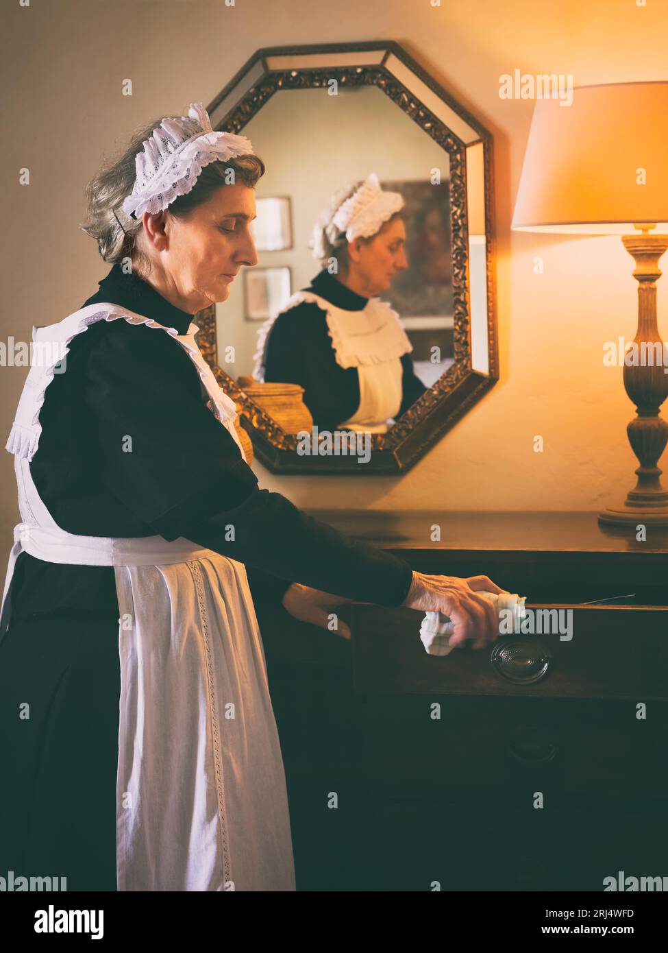 Viktorianische Dienstmädchen oder Diener in schwarzem Kleid, Spitzenkappe und weißer Schürze, die in einem Interieur aus dem 19. Jahrhundert arbeiten Stockfoto