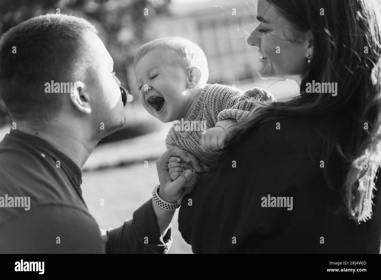 Glückliche Familie in einem Park. Dad hält Dummy in den Mund. Mutter, die ihren Sohn hält und versucht, einen Schnuller auszuziehen. Hochwertige Fotos Stockfoto