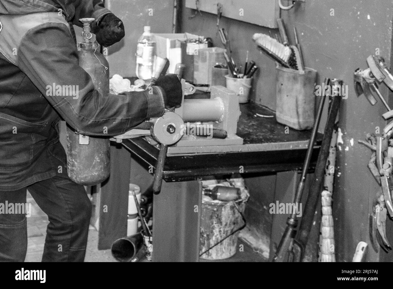 Ein männlicher Arbeiter auf einem großen industriellen Schraubstock aus Metall repariert einen roten Feuerlöscherzylinder in einer Werkstatt im Werk. Stockfoto