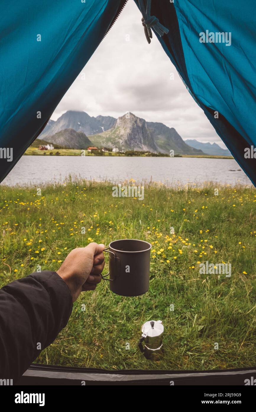 Die Hand des Mannes hält einen Becher in einem Campingzelt mit Seeblick in Norwegen Stockfoto