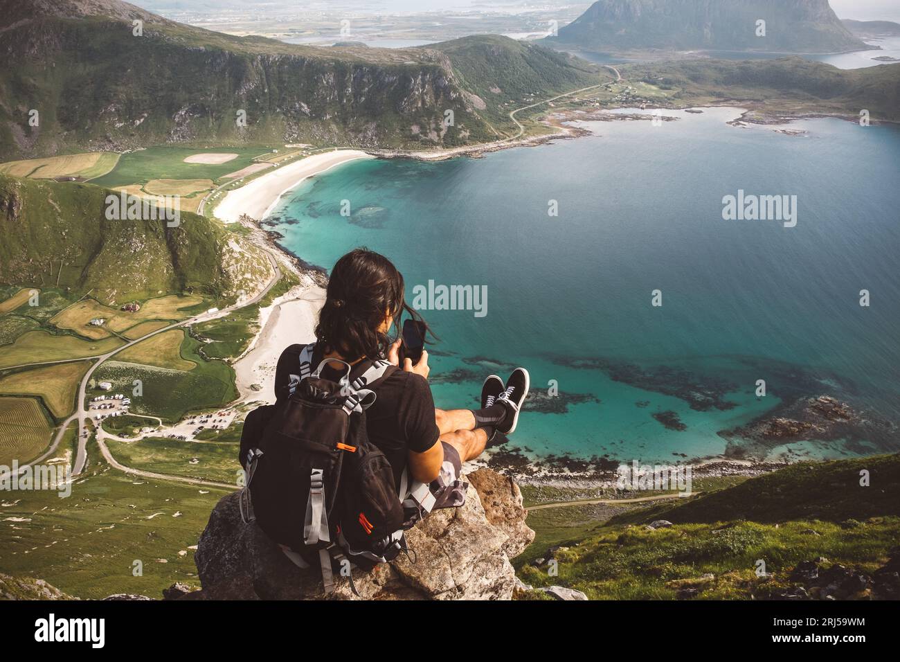 Mann mit einem Handy sitzt in einem Felsen und macht Fotos von der Aussicht Stockfoto