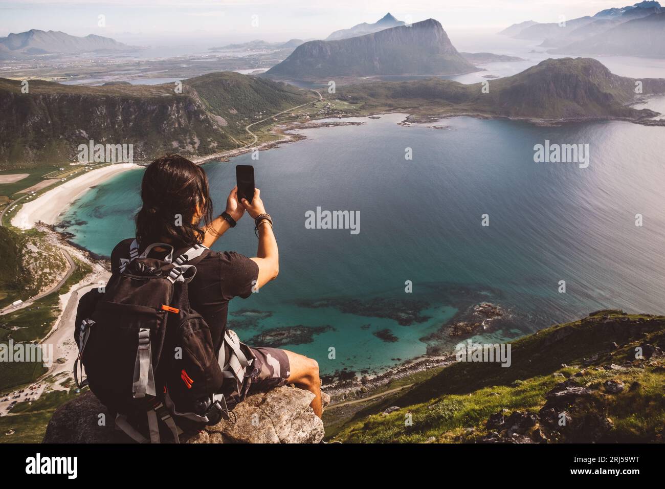 Mann mit einem Handy sitzt in einem Felsen und macht Fotos von der Aussicht Stockfoto
