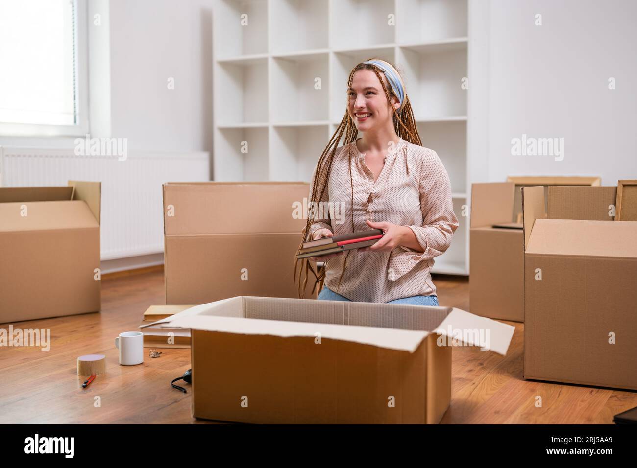 Moderne Ingwerfrau mit Zöpfen zieht in ein neues Zuhause. Stockfoto