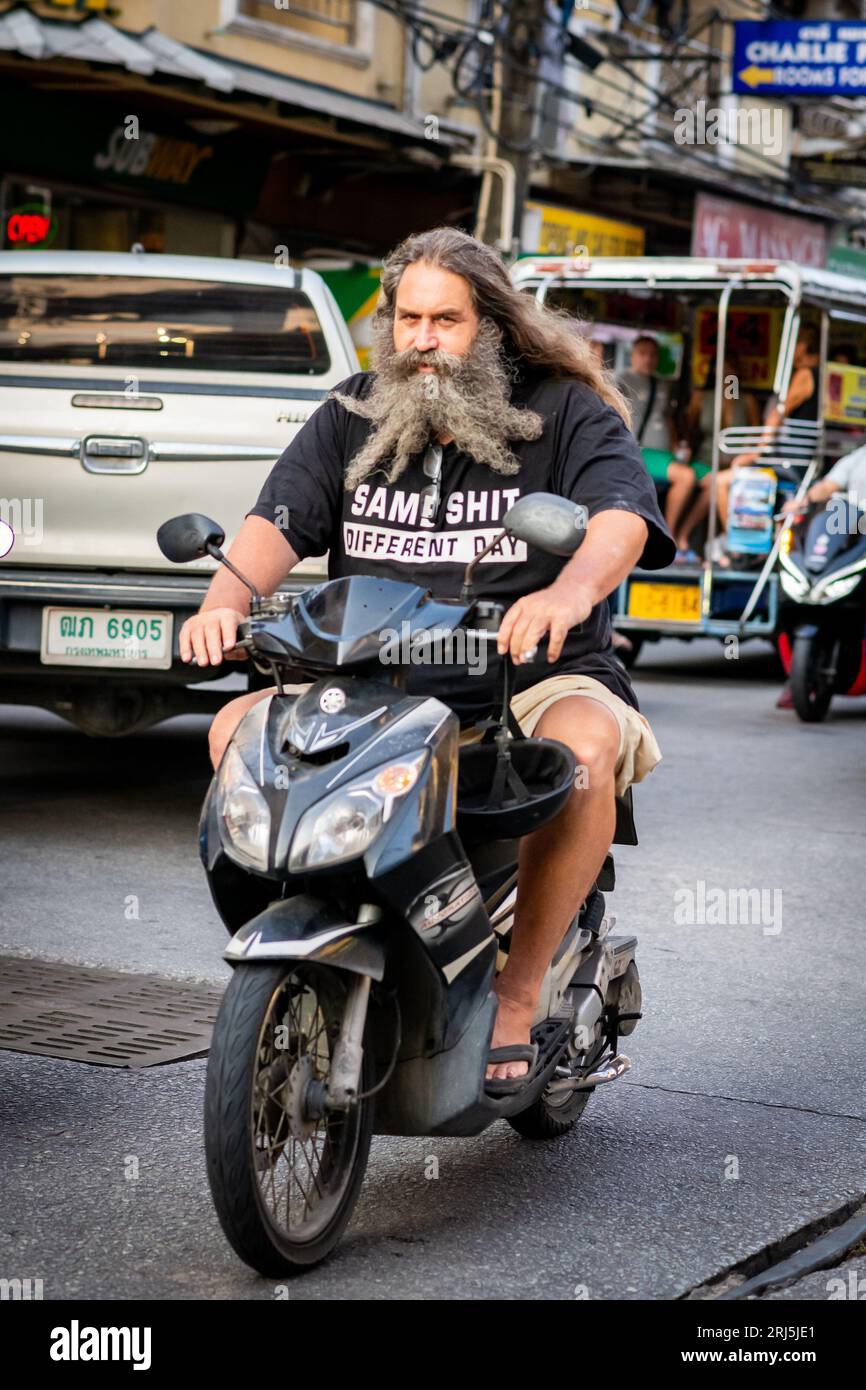 Ein Mann mit einem sehr langen Bart macht sich auf seinem Roller auf den Weg entlang Soi Buakhao, Pattaya, Thailand. Stockfoto