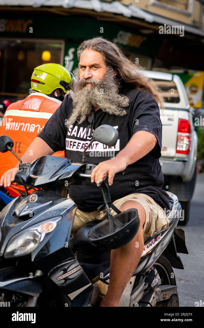 Ein Mann mit einem sehr langen Bart macht sich auf seinem Roller auf den Weg entlang Soi Buakhao, Pattaya, Thailand. Stockfoto