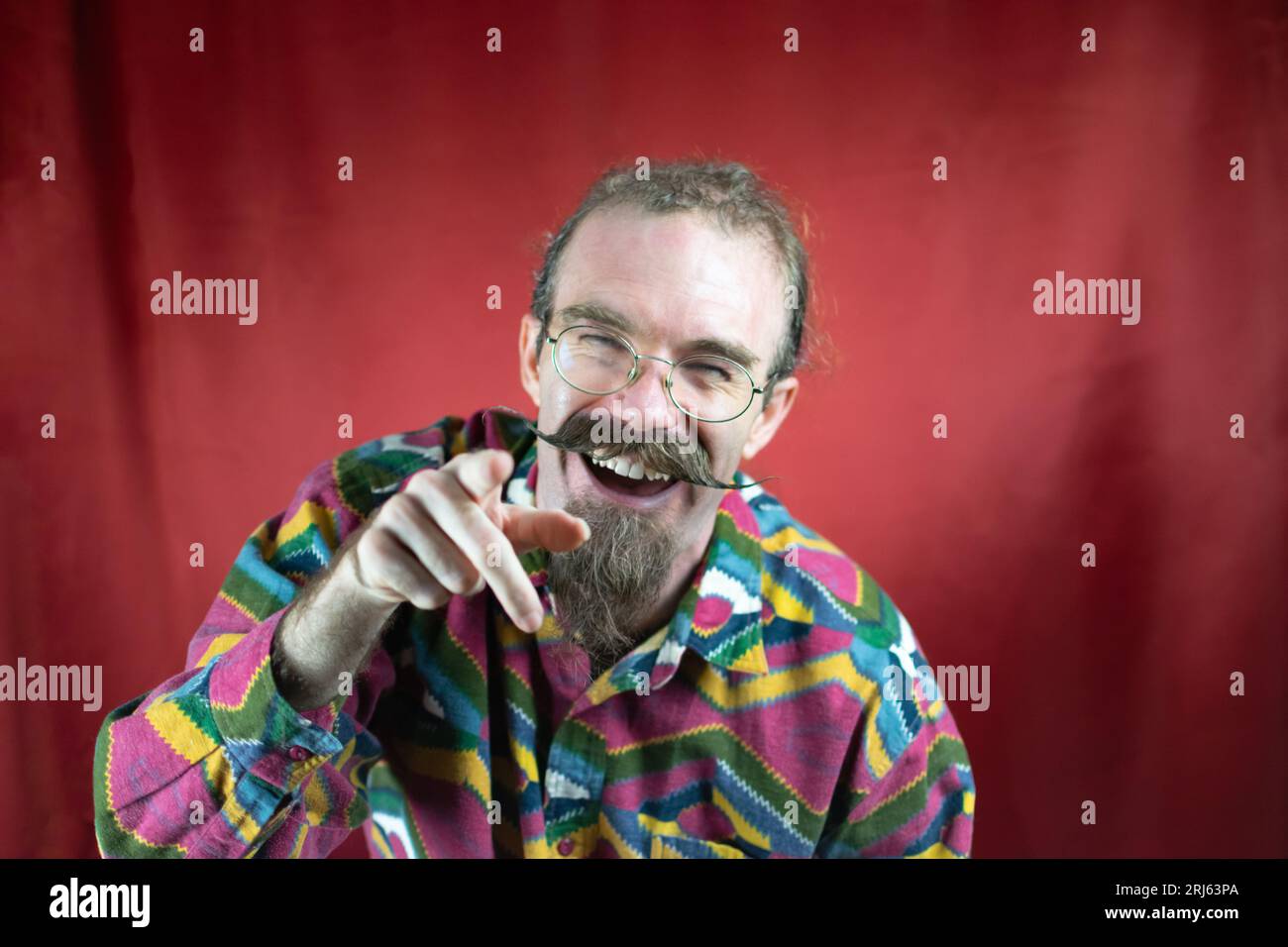Hipster-Mann mit Brille und Schnurrbart zeigt auf Kamera lachend und neckend Stockfoto