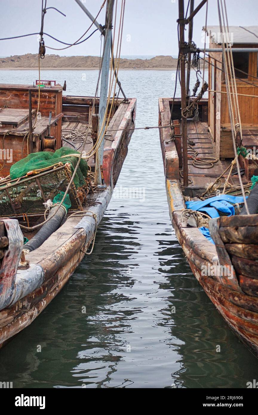 Zwei traditionelle Fischereifahrzeuge, die sicher an einem Dock festgemacht sind, liegen nebeneinander in einem ruhigen Gewässer Stockfoto