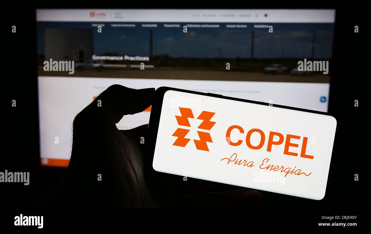 Person, die ein Mobiltelefon mit dem Logo der Firma Companhia Paranaense de Energia (Copel) auf dem Bildschirm vor der Webseite hält. Konzentrieren Sie sich auf das Display des Telefons. Stockfoto