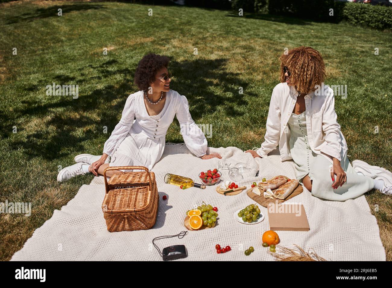 Positive afroamerikanische Freundinnen in der Nähe von Obst, Gemüse auf Decke, Sommerpicknick Stockfoto