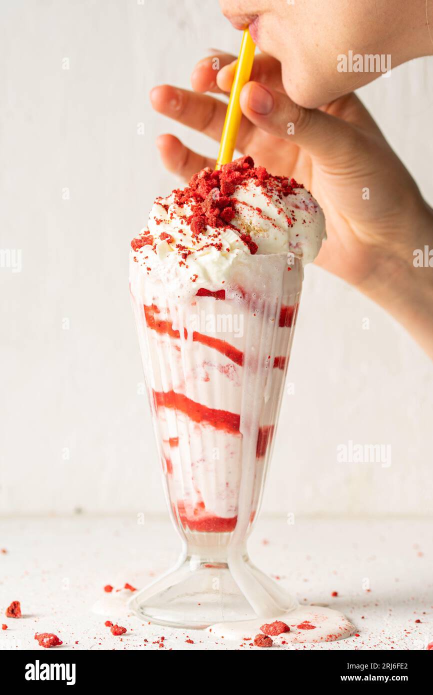 Die Hand eines Menschen hält einen Orangenstroh und trinkt cremigen Erdbeermilchshake Stockfoto