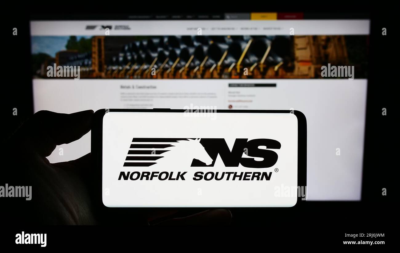 Person, die ein Mobiltelefon mit dem Logo der US-Eisenbahngesellschaft Norfolk Southern Corp. Auf dem Bildschirm vor dem Firmenlogo hält. Konzentrieren Sie sich auf das Display des Telefons. Stockfoto