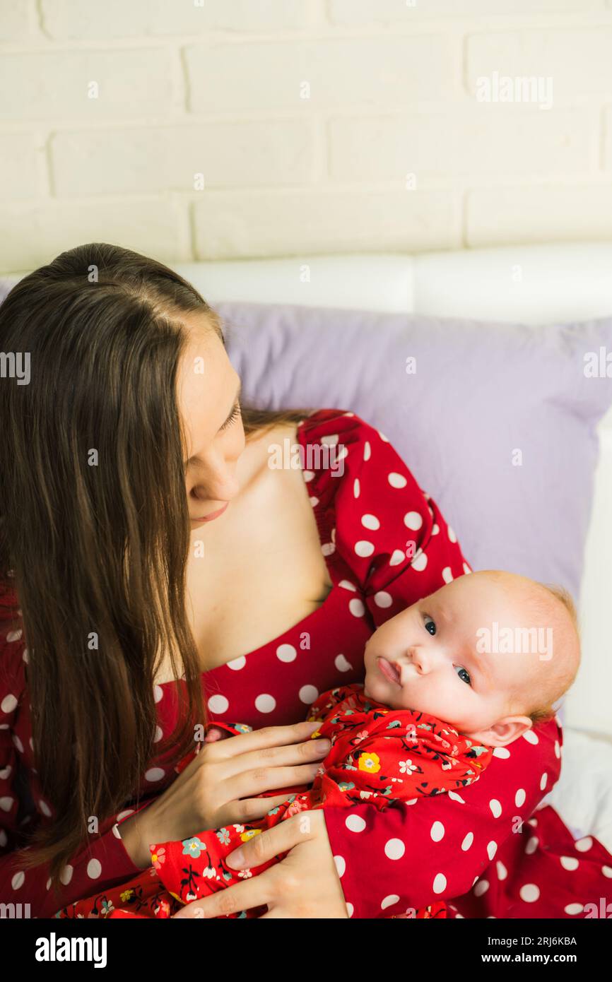 Neugeborenes Mädchen an den Händen der Mutter in rotem Polka-Dot-Kleid Stockfoto