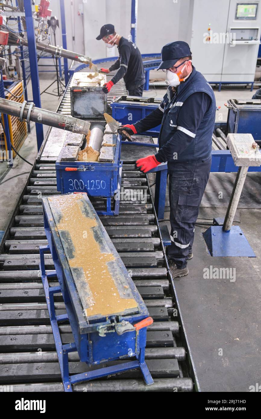 Werkarbeiter schüttet Zementmischung in eine Form und glättet sie mit einem Werkzeug. Stockfoto