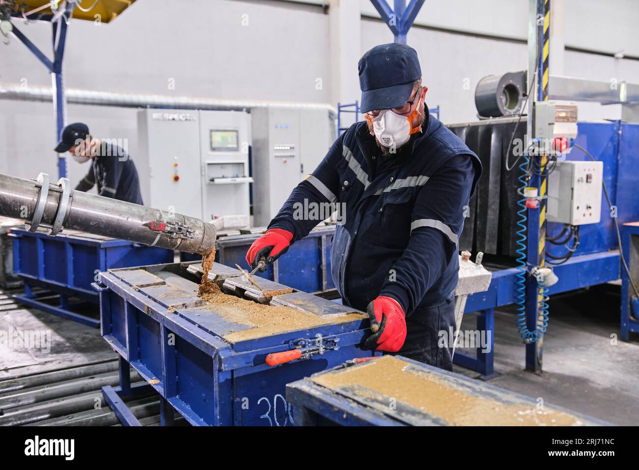 Werkarbeiter schüttet Zementmischung in eine Form und glättet sie mit einem Werkzeug. Stockfoto