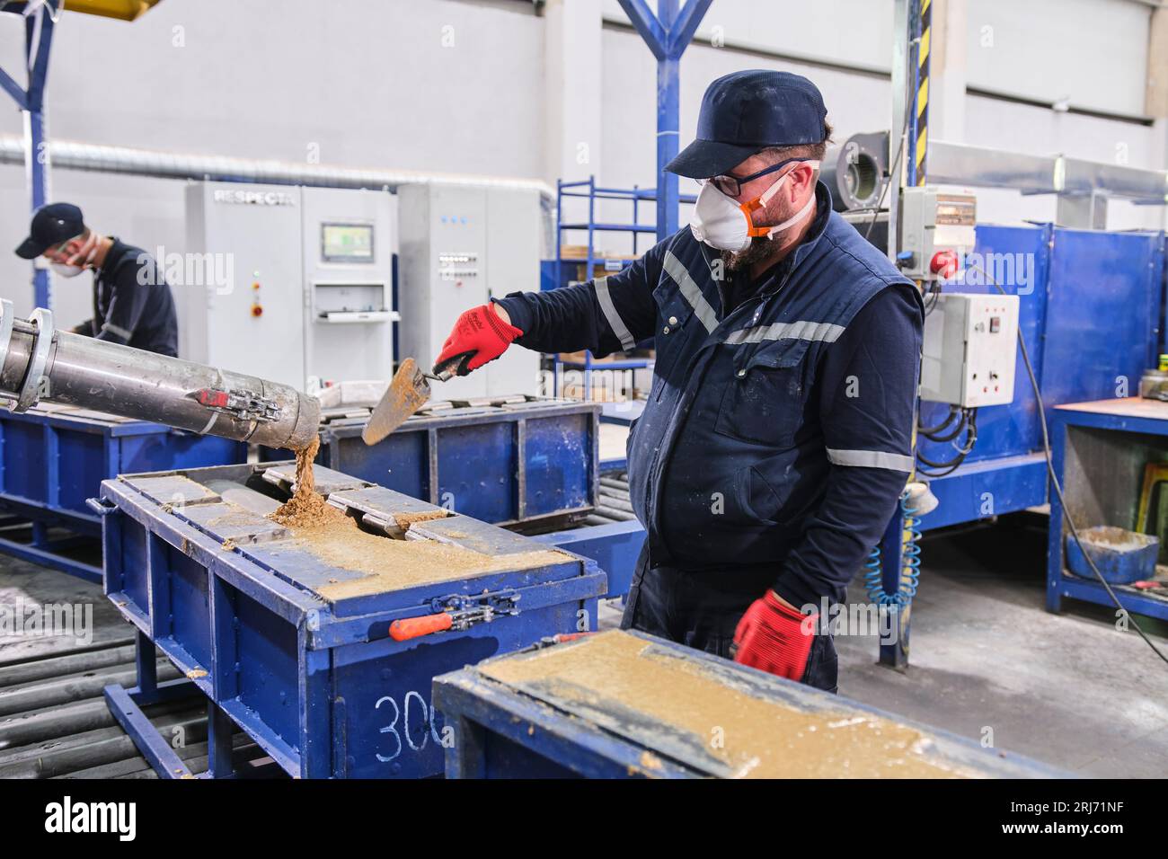 Werkarbeiter schüttet Zementmischung in eine Form und glättet sie mit einem Werkzeug. Stockfoto