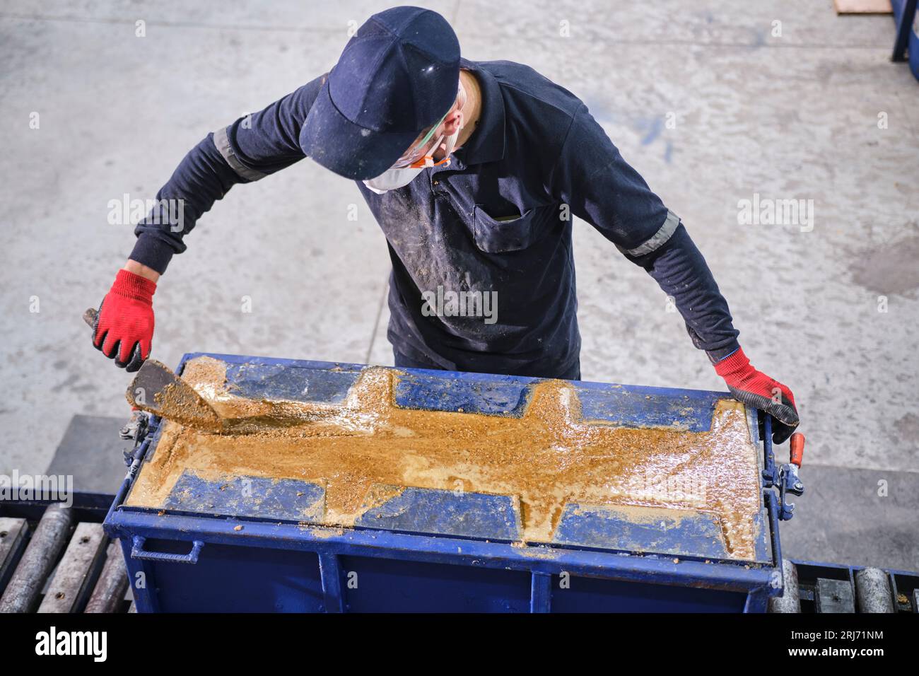 Werkarbeiter schüttet Zementmischung in eine Form und glättet sie mit einem Werkzeug. Stockfoto