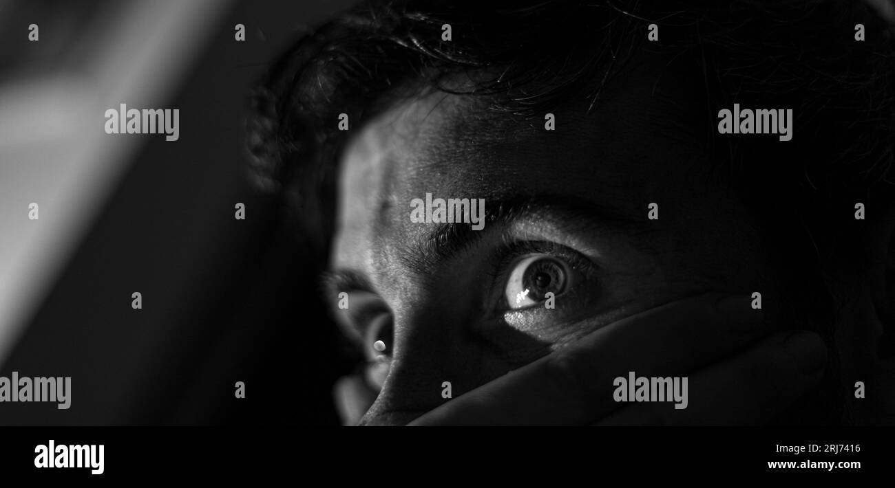 Graustufenaufnahme der traurigen Augen eines jungen Mannes in dunkler Umgebung Stockfoto