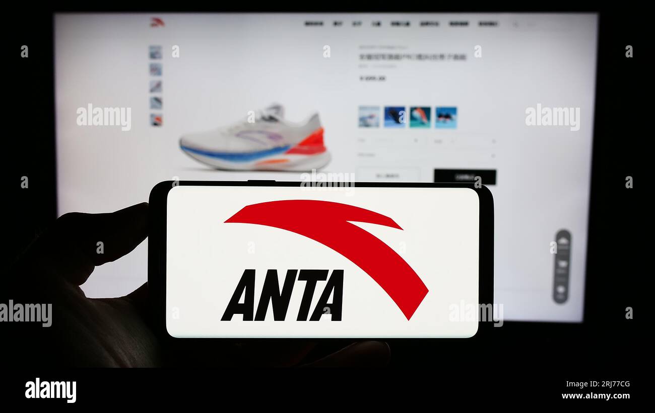 Person, die ein Mobiltelefon mit dem Logo des chinesischen Unternehmens Anta Sports Products Limited auf dem Bildschirm vor der Webseite hält. Konzentrieren Sie sich auf das Display des Telefons. Stockfoto