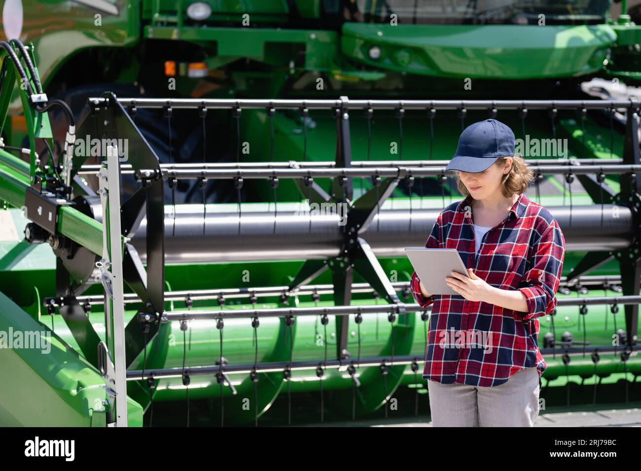 Landwirtin mit digitalem Tablet vor dem Hintergrund der Erntemaschine. Konzept der intelligenten Landwirtschaft. Stockfoto