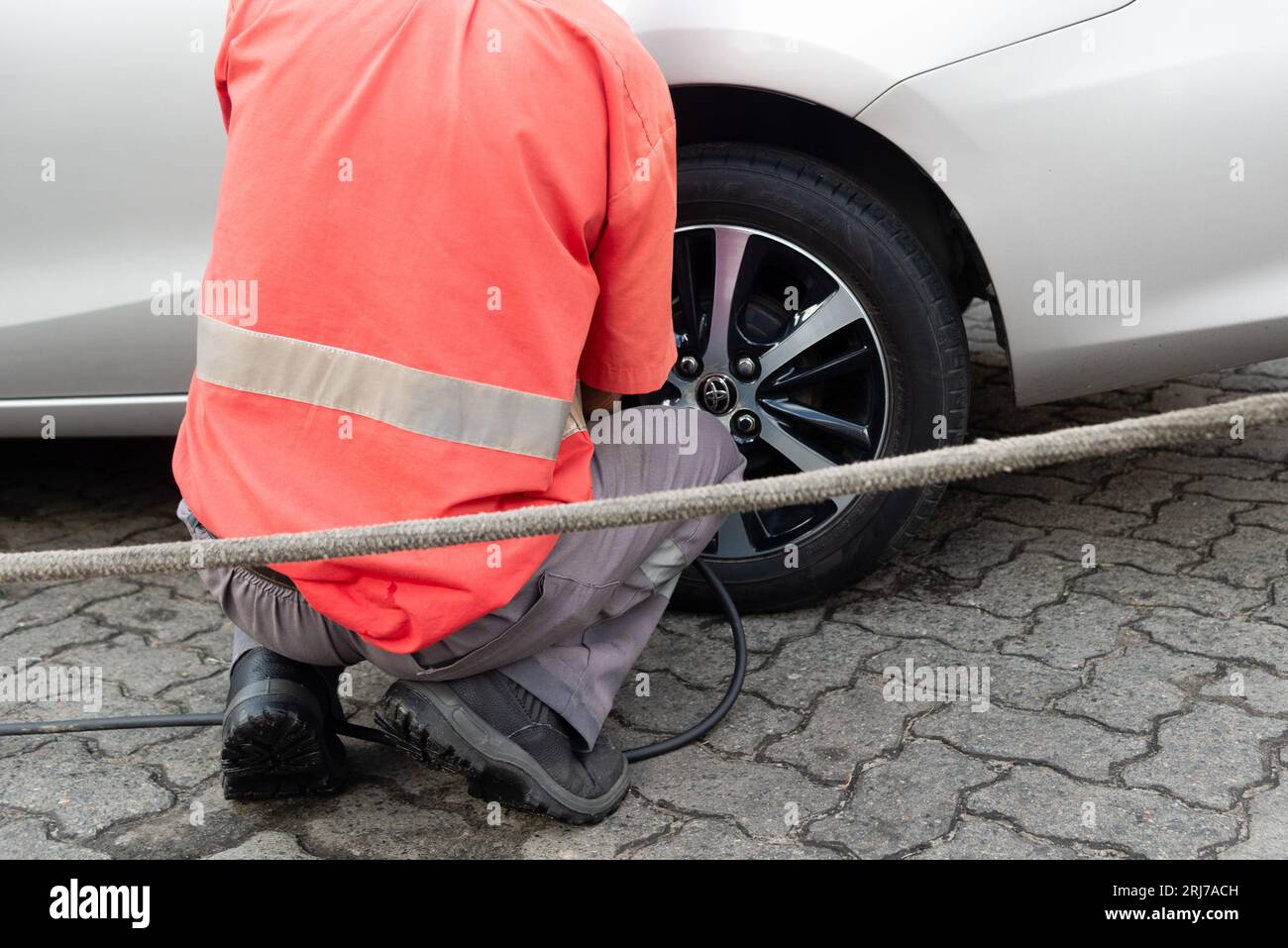 Salvador, Bahia, Brasilien - 11. August 2023: Ein Tankstellenarbeiter wird gesehen, wie er einen Autoreifen auf der Avenida Tancredo Neves aufpumpt. Stadt Salvador, Bahia. Pumpe Stockfoto