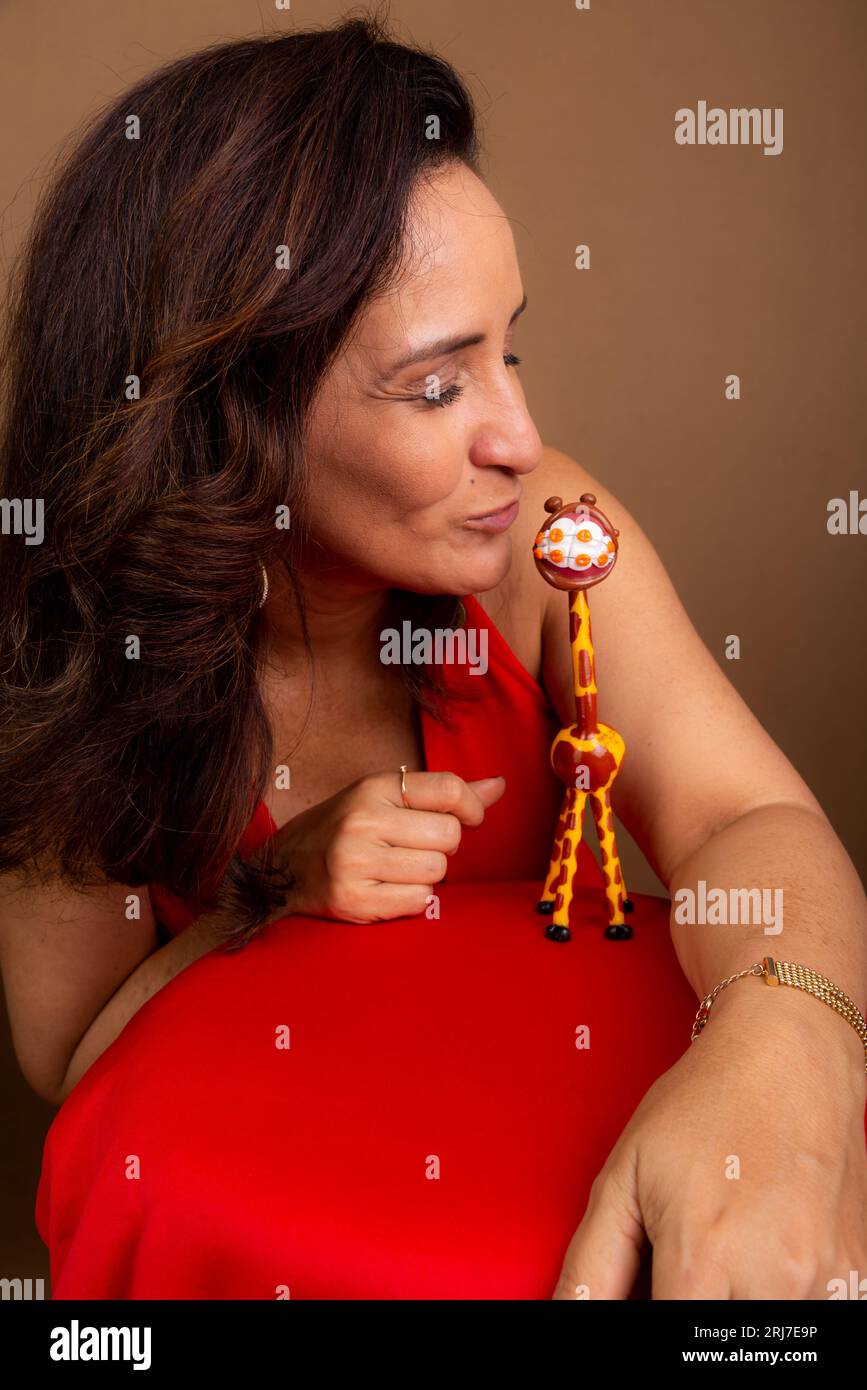 Eine fröhliche Trainerin, die eine Giraffen-Puppe küsst. Symbol für gewaltfreie Kommunikation. Isoliert auf braunem Hintergrund. Stockfoto