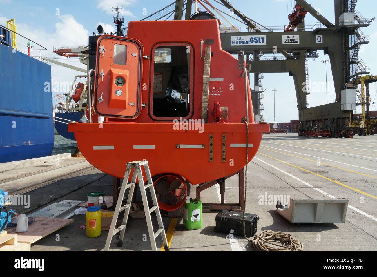 Orangefarbenes Rettungsboot mit offener Hecktür, die repariert wird und an der Ladestation an Land im Containerterminal in Kingston befestigt ist. Stockfoto