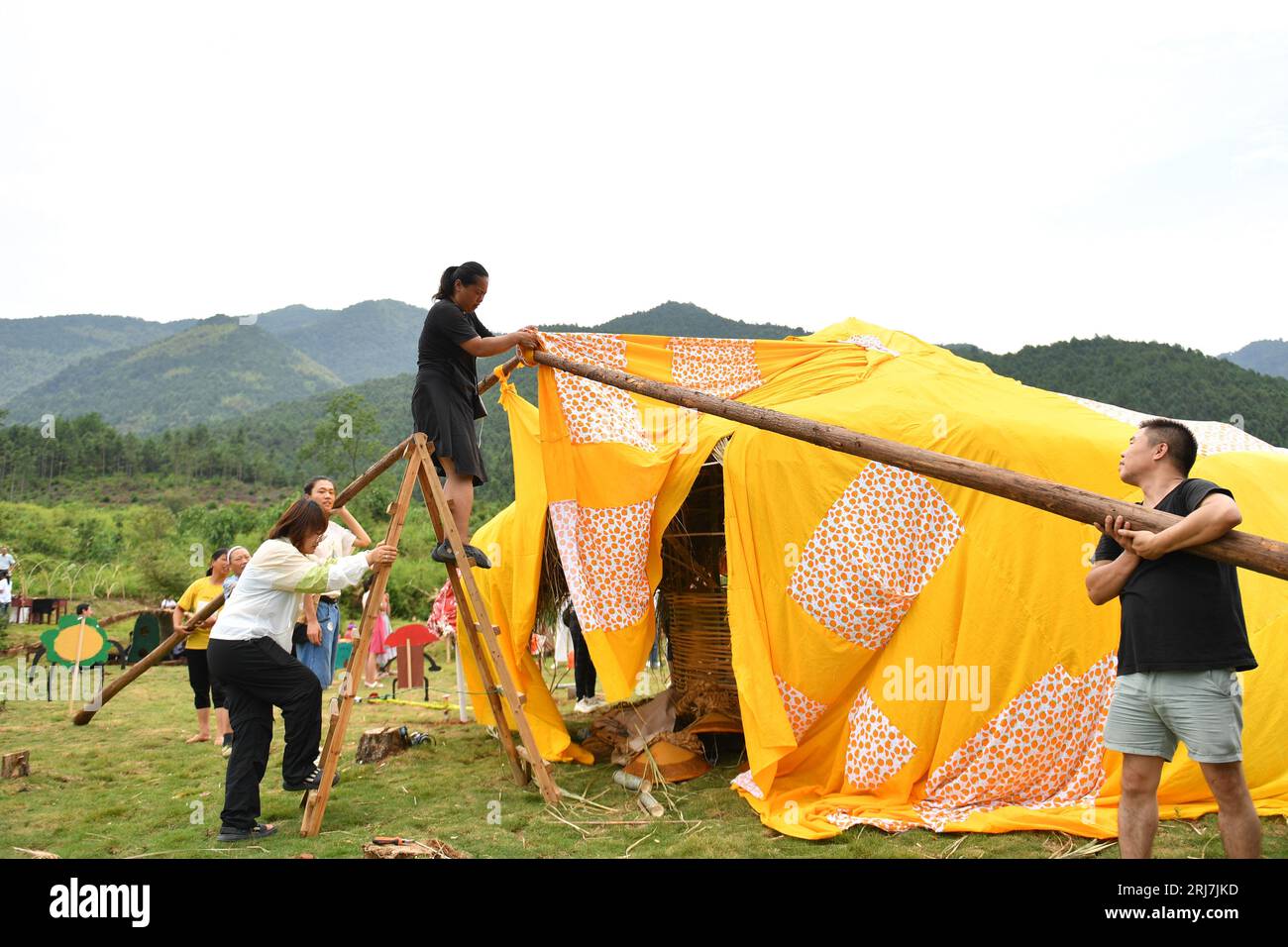 (230821) -- NINGYUAN, 21. August 2023 (Xinhua) -- Zhou Yan verbindet zwei Balken, als sie mit Hilfe von Freiwilligen und Dorfbewohnern eine Kunstinstallation in der Provinz Ningyuan in der zentralchinesischen Provinz Hunan am 20. August 2023 aufbaut. Liu Xiu und seine Frau Zhou Yan gründeten 2015 ein Kunst- und Kulturaustauschzentrum für Kinder im Dorf Youyujing in der Township Shuishi im County Ningyuan der zentralchinesischen Provinz Hunan. Seitdem bieten das Paar und einige ortsansässige Lehrer Kunstkurse für Kinder aus dem Dorf und den Nachbarstädten an. Mehr als 50 Kinder pro Person Stockfoto