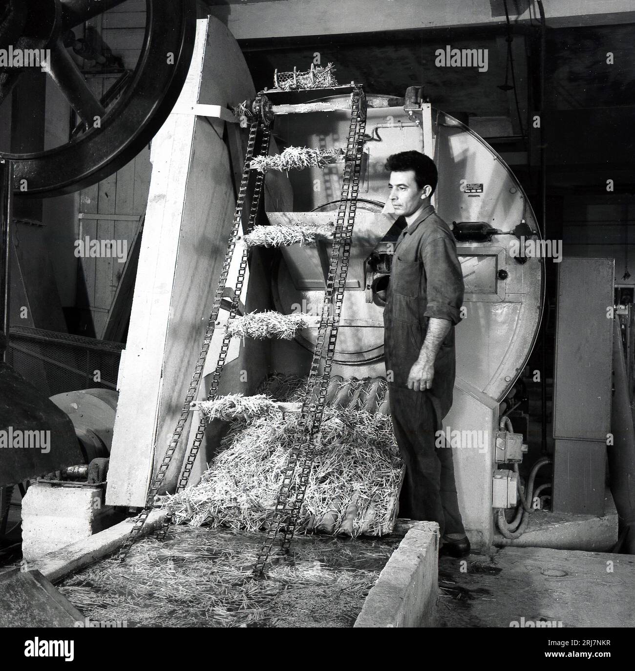 1950er Jahre, historisch, ein männlicher Arbeiter, der in einer landwirtschaftlichen Fabrik neben einer Maschine mit dem Fabrikschild von A. Roller aus Berlin steht. Stockfoto