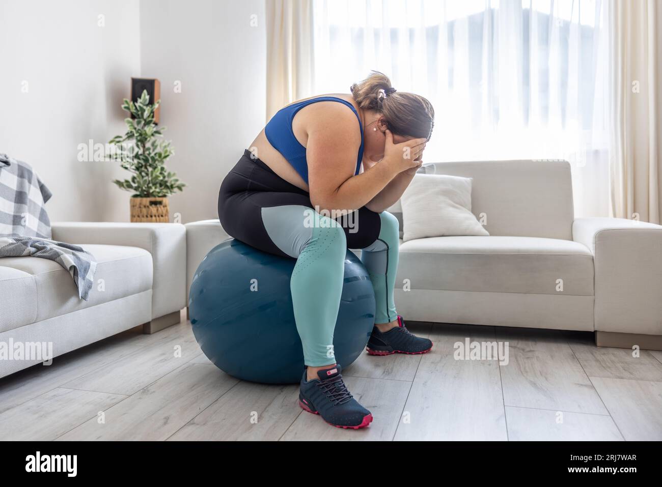 Frustrierte adipöse Frau, die auf einem schweizer Ball sitzt und wegen ihres Übergewichts weint. Stockfoto