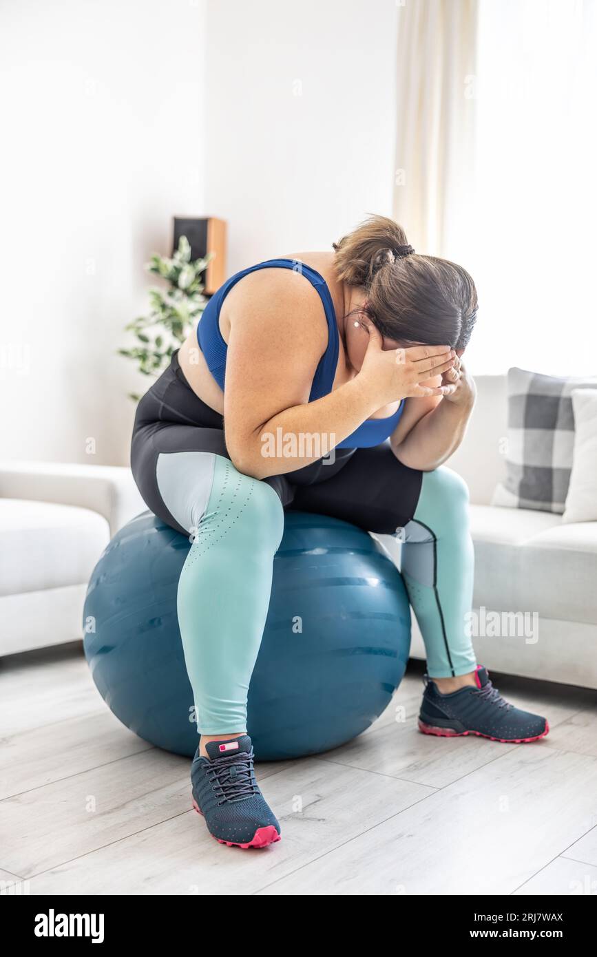 Frustrierte adipöse Frau, die auf einem schweizer Ball sitzt und wegen ihres Übergewichts weint. Stockfoto