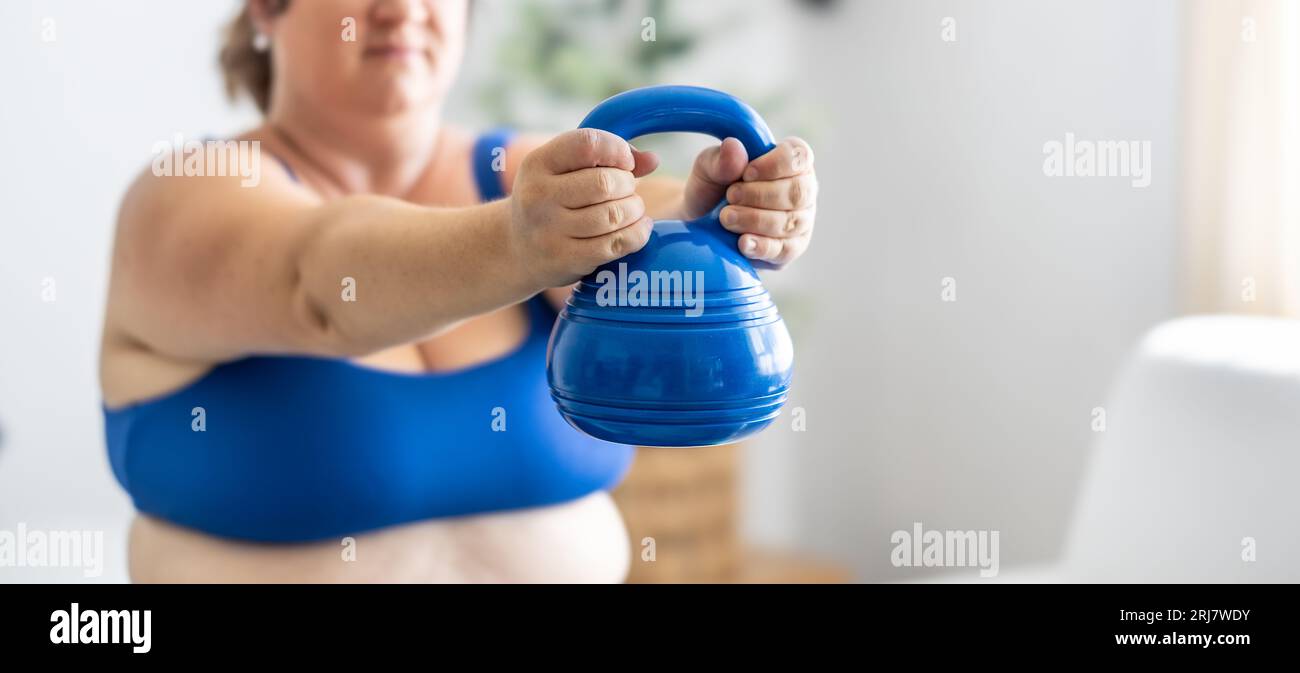 Plus Größe Frau, die Übungen mit Kurzhanteln macht, ihren Körper im Wohnzimmer stärkt, selektive Fokussierung. Stockfoto