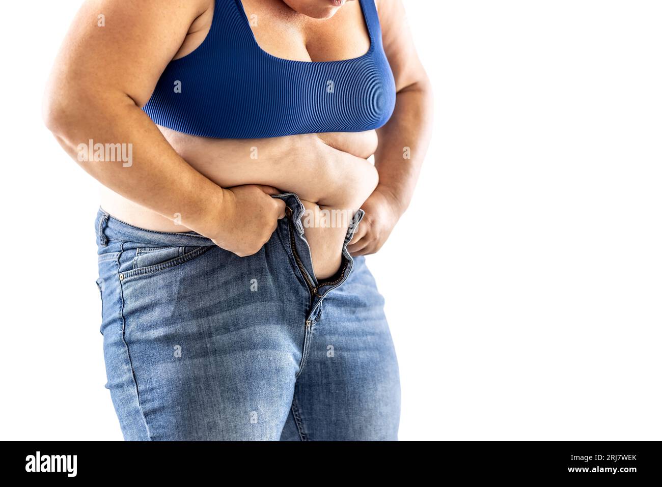 Eine fette Frau hat Schwierigkeiten, ihre Jeans zu knöpfen - isoliert auf weiß. Stockfoto