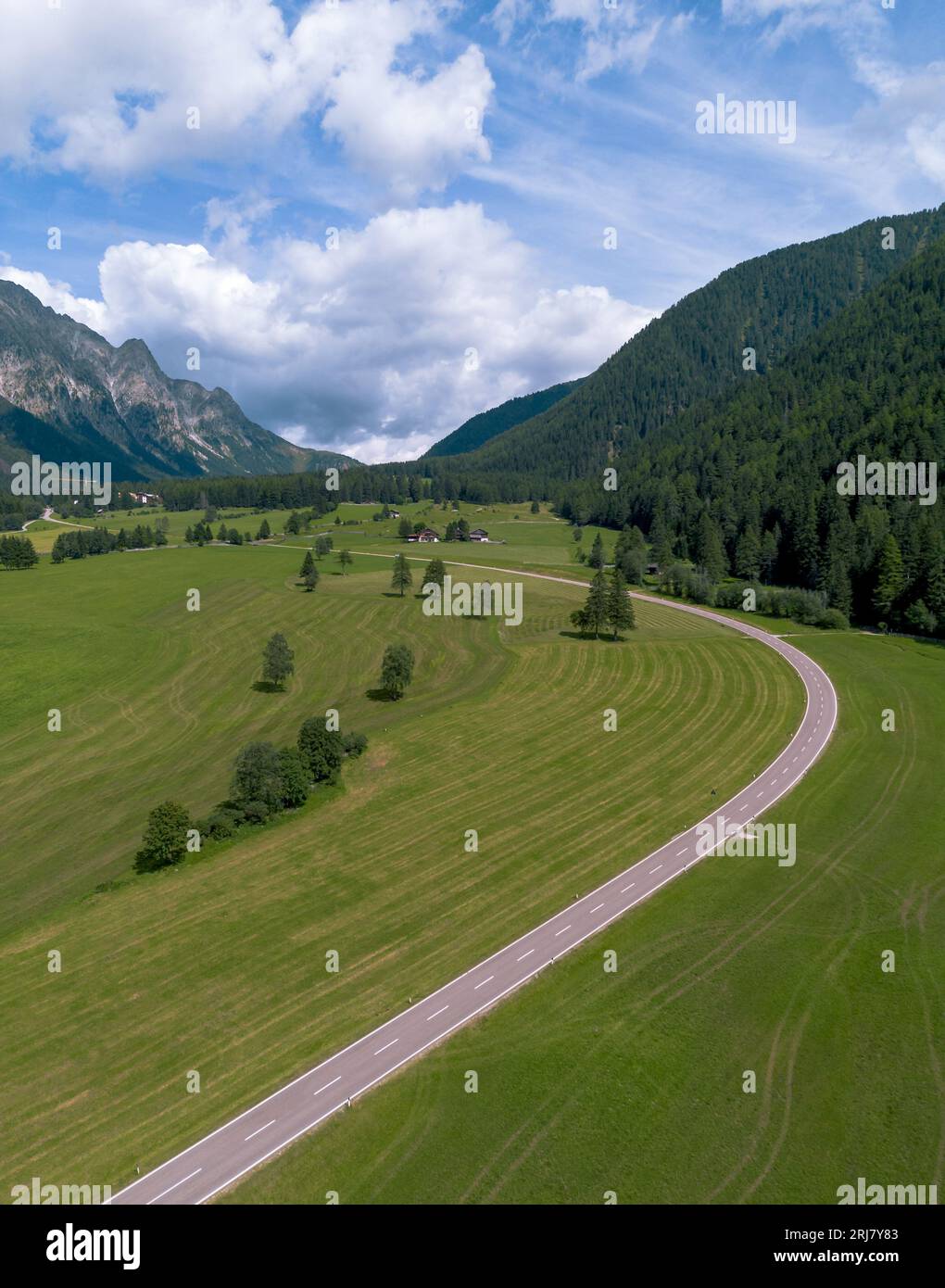 Schmale Asphaltstraßenkurve in grüner landwirtschaftlicher Landschaft im Bergtal in den italienischen Dolomiten Stockfoto