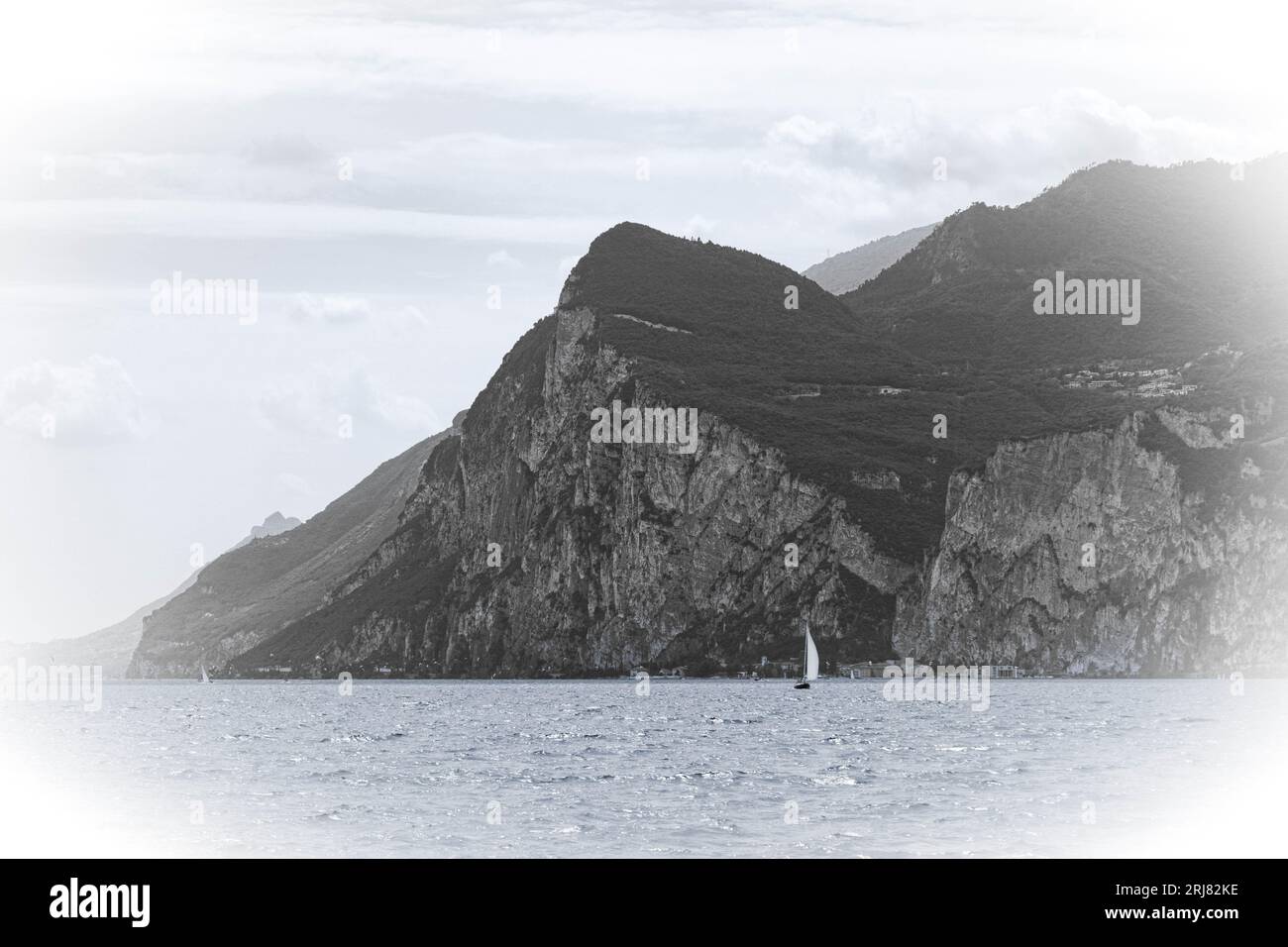 Schwarz-weiß-Foto mit weißer Vignette des Gardasees und Berges mit einem Segelboot Stockfoto