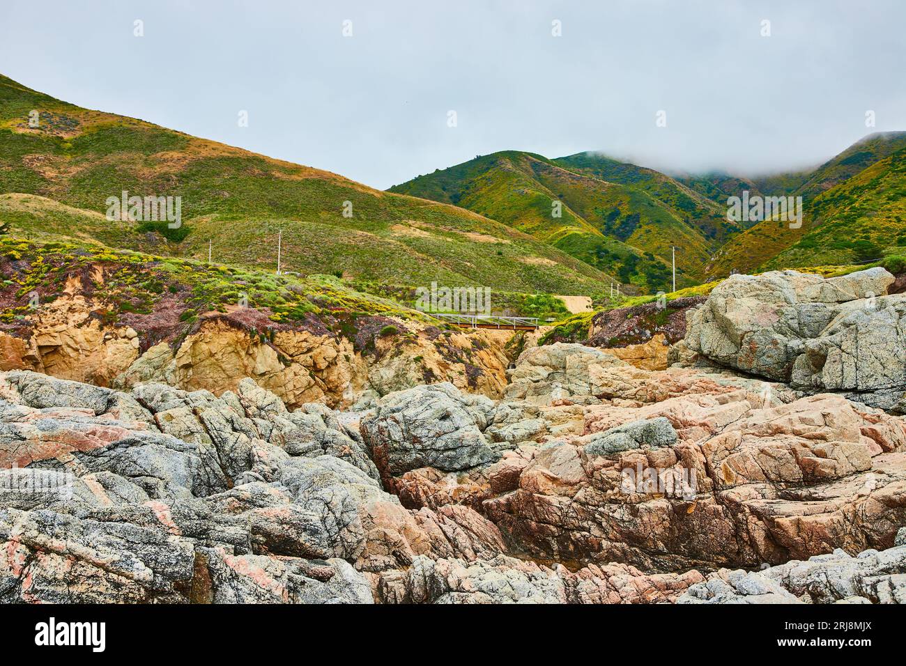 Baren-Felsklippen mit zerklüfteten Felsen und fernen grünen Berghügeln unter bedecktem Himmel Stockfoto