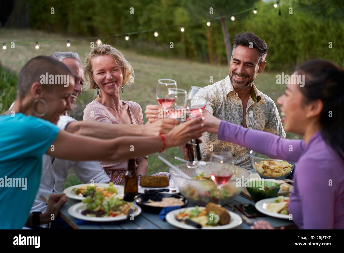 Gruppe von Freunden mittleren Alters, die gemeinsam auf der Terrasse eines Hauses oder Restaurants speisen. Glückliche Menschen essen und trinken Toast an einem Tisch im Freien Stockfoto